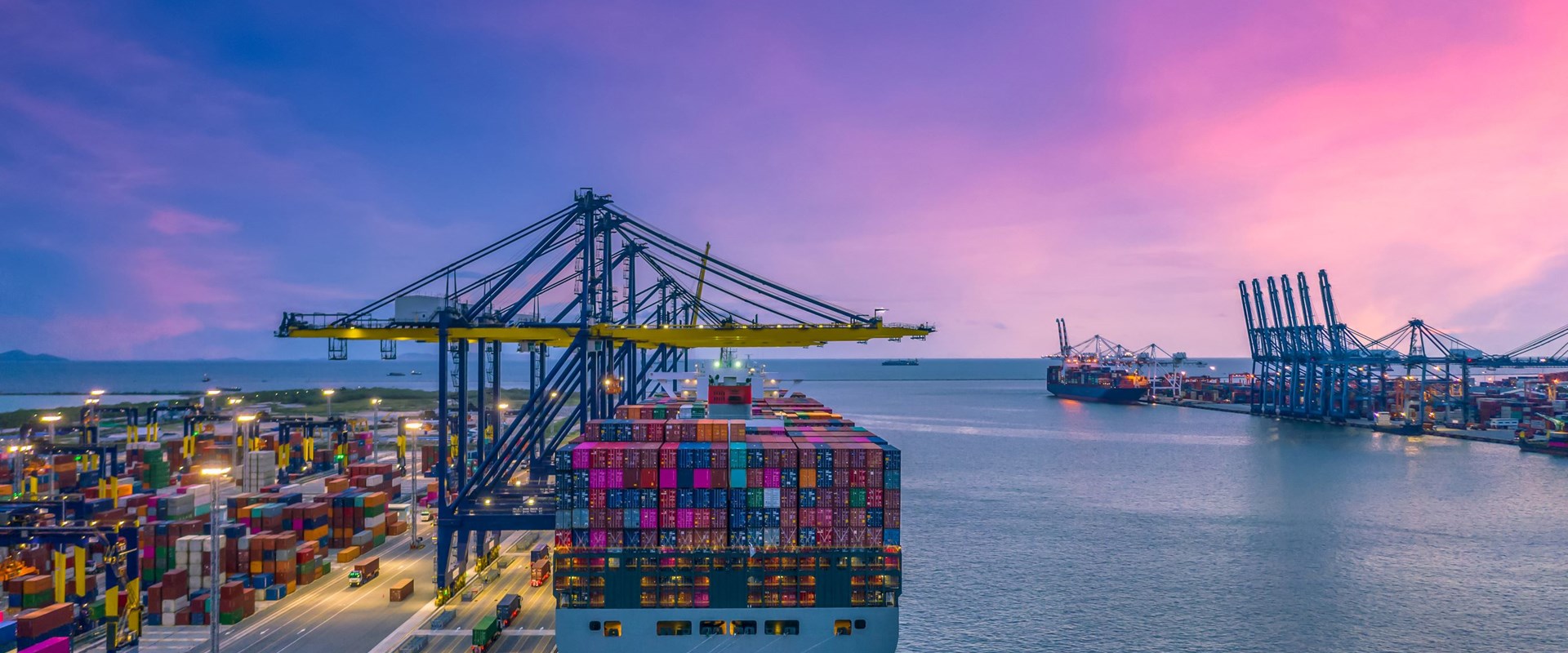 Container ship being unloaded by a crane in port, with a deep purple sky