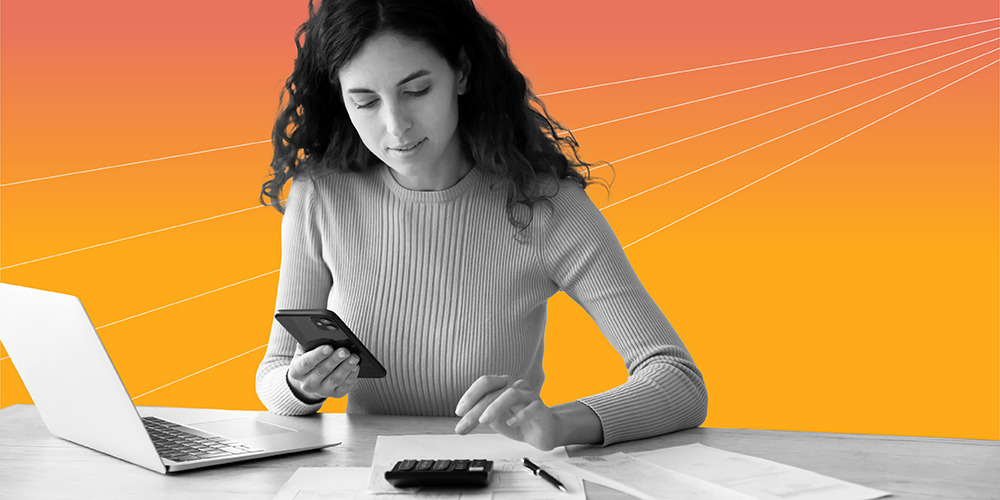 young woman with long curly hair working at desk with her laptop, phone, and calculator