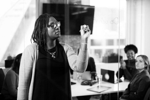 Woman writing notes on glass during team meeting